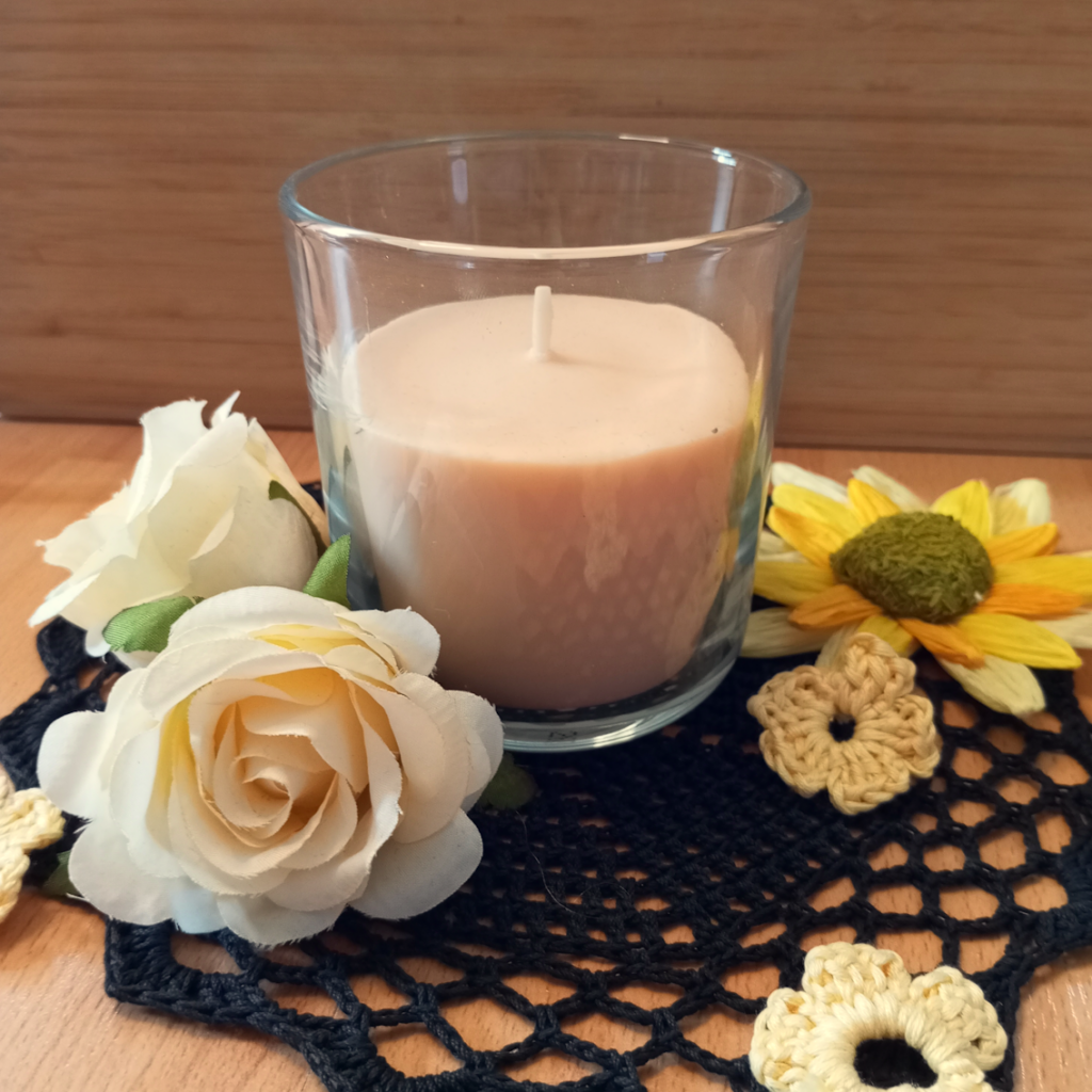 Eine Duftkerze auf einem schwarzen Zierdecken mit künstlichen Blumen dekoriert