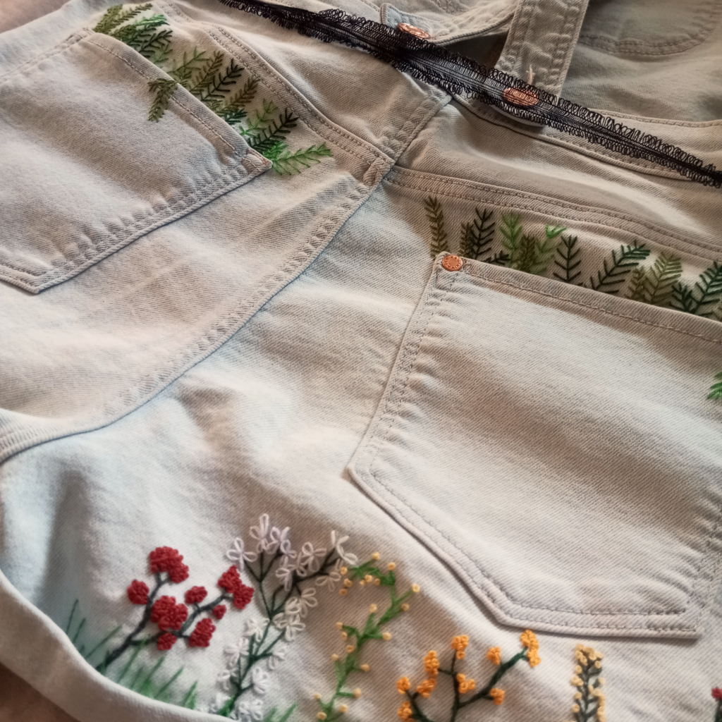 Nahaufnahme von gestickten, bunten Blumen auf einer Latzhose