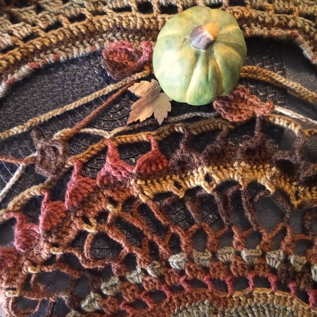 Häkelarbeit in herbstlichen Farben und einem grünen Kürbis zur Deko
